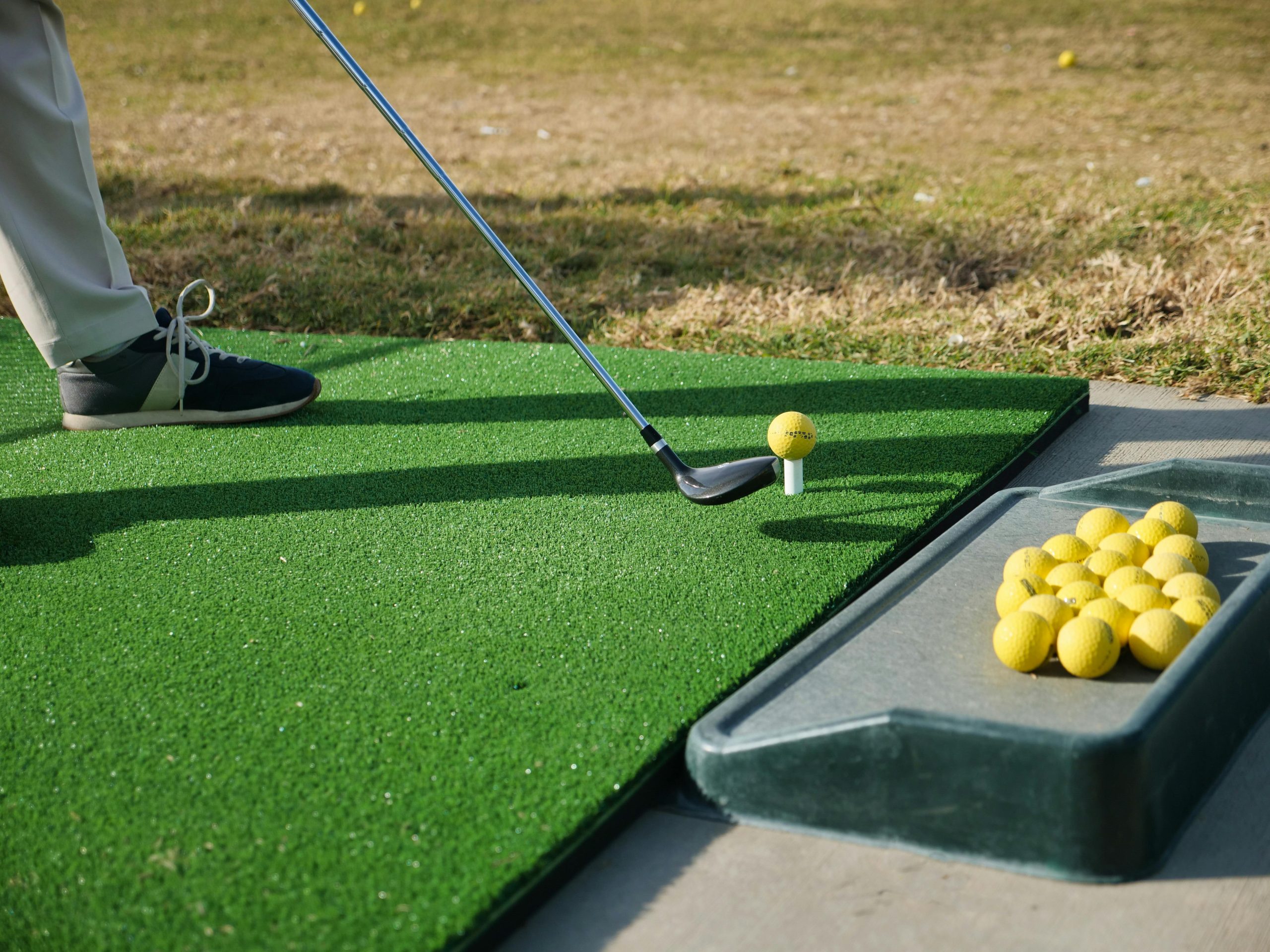 Golfer practicing at a driving range hitting a teed ball with alignment and repetition drills to fix a slice