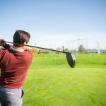 Golfer finishing a driver swing on a fairway, viewed from behind, suitable for illustrating ball flight direction in a push slice shot