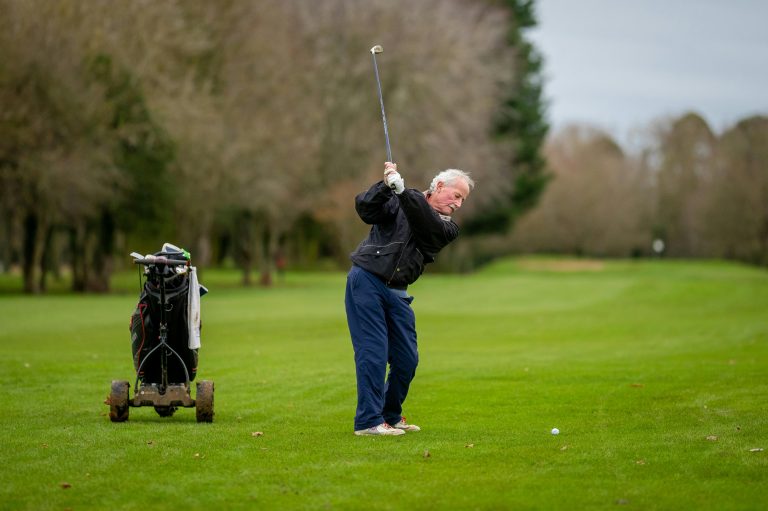 Golfer mid downswing with an outside-in swing path on a fairway, demonstrating over-the-top motion causing a slice