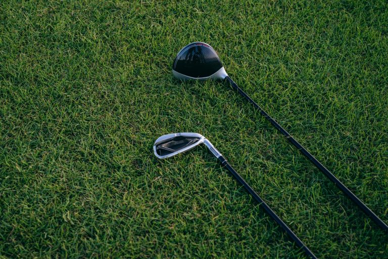 Golf driver and iron lying on grass, illustrating differences between clubs that can cause a driver slice