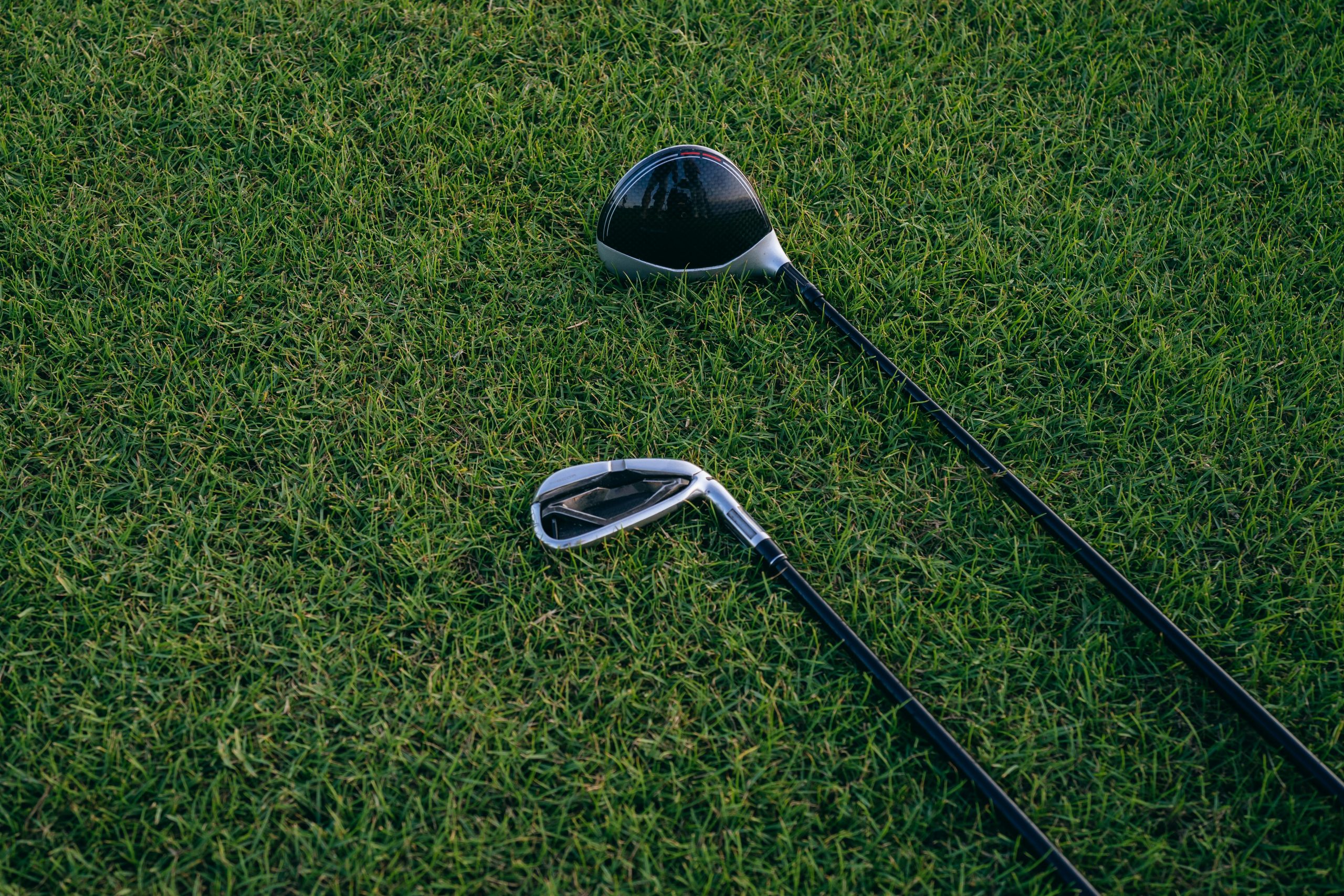 Golf driver and iron lying on grass, illustrating differences between clubs that can cause a driver slice